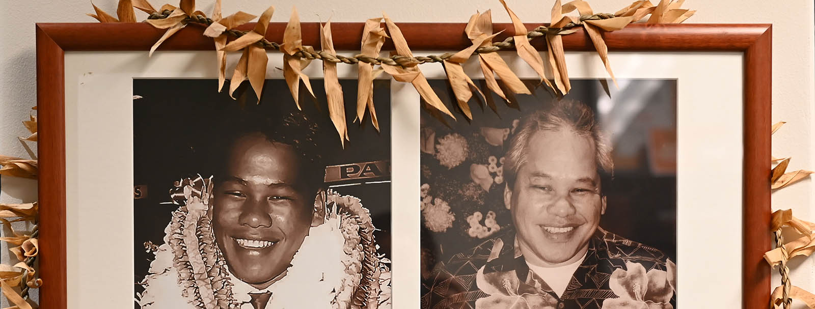 A framed collage displays two sepia-toned photos of Warren Ah Loo smiling, adorned with leis, hung on a wall. A dried, woven lei made of leaves is draped over the top of the wooden frame. The background behind the frame is a plain, light-colored wall. This image is featured on the "Our Story " page of the Nakupuna Foundation website. The Nakupuna Foundation is a Native Hawaiian Owned non-profit.