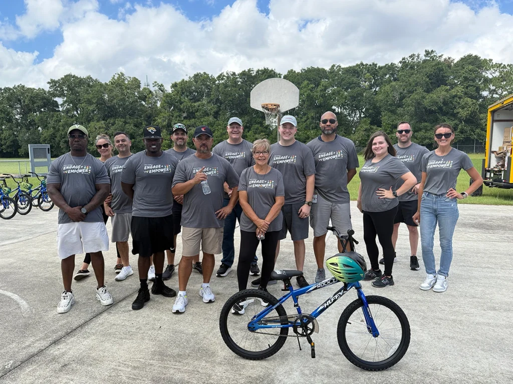 Our News 5 Group of volunteers with "engage empower" shirts stand with a blue kids' bicycle on a basketball court.